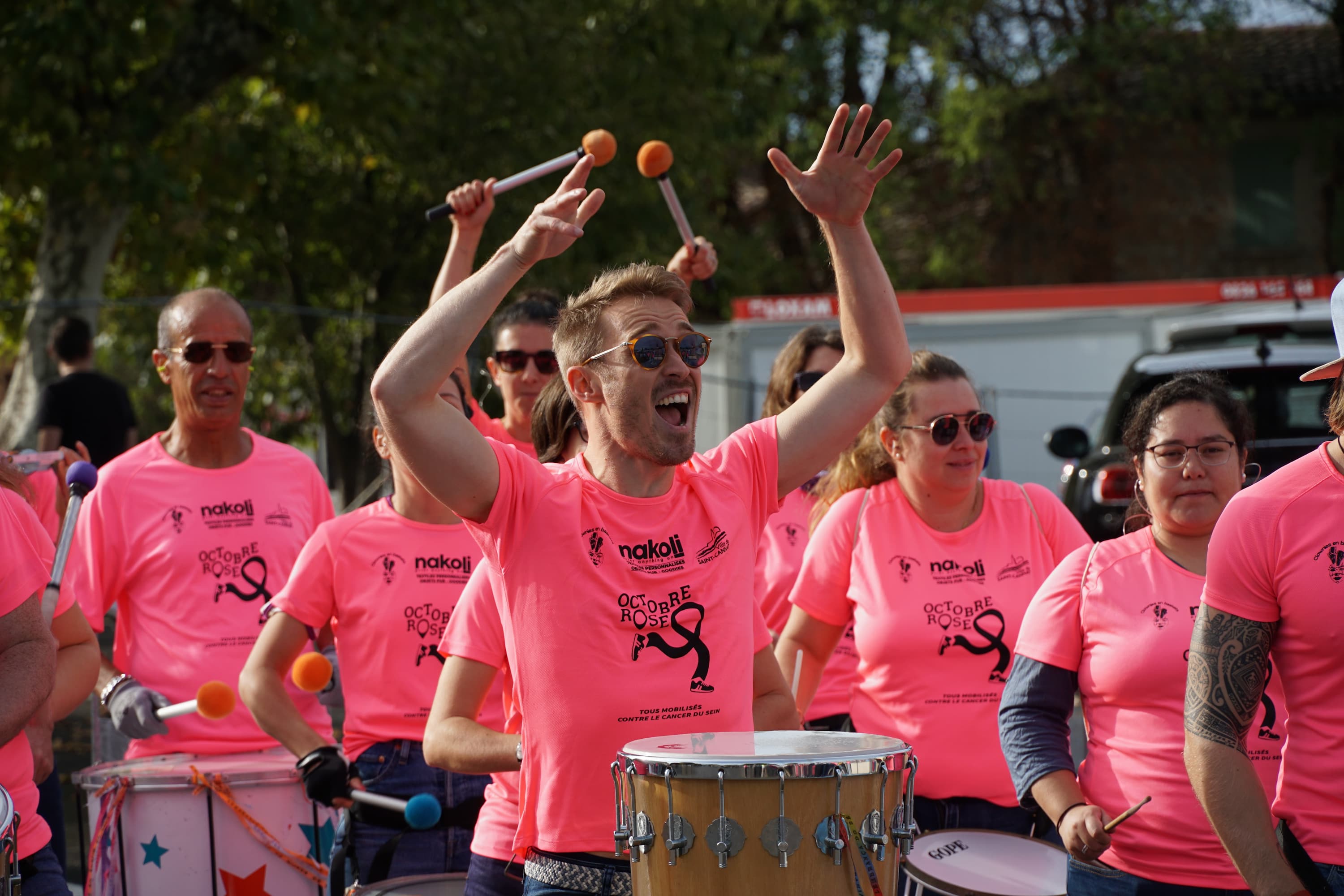 Plusieurs personne avec des t-shirts rose "Octobre Rose" qui défilent avec des instruments de musique